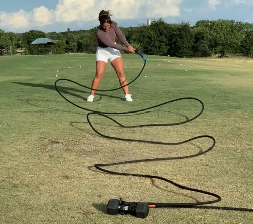 A woman swinging a Mach3 golf speed training tool outside on a golf course.